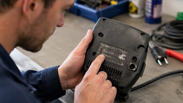 e-check.nrw – EinElektriker schaut sich das Typenschild auf einem Elektro-Kleingerät an. Sichtprüfung bei einer DGUV V3 Prüfung.